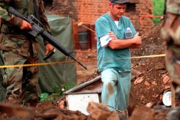 U.S. Marines provide security as members of the Royal Canadian Mounted Police Forensics Team investigate a grave site in a village in Kosovo on July 1, 1999.