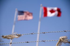 Image of Canadian and US flags flying behind barbed wire