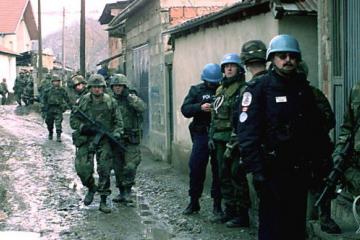 U.S. Army soldiers and United Nations’ police move down a muddy alley way in Mitrovica, Kosovo, as they conduct a house-to-house search for weapons on Feb. 21, 2000.